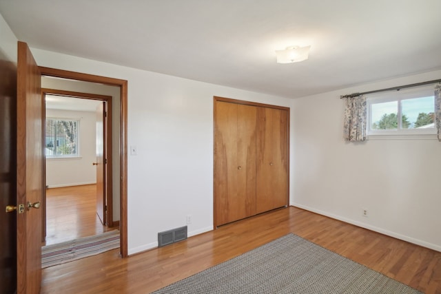 unfurnished bedroom featuring multiple windows, light wood-type flooring, and a closet