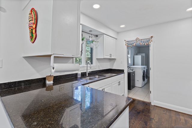 kitchen with dark stone counters, wood-type flooring, sink, separate washer and dryer, and white cabinetry