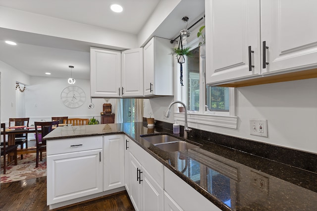 kitchen featuring sink, kitchen peninsula, dark stone countertops, dark hardwood / wood-style flooring, and white cabinetry