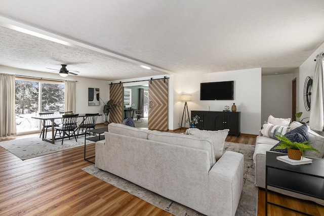 living area with a ceiling fan, wood finished floors, a textured ceiling, and a barn door