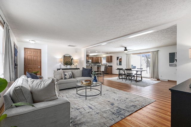 living area featuring visible vents, baseboards, a ceiling fan, light wood-style flooring, and a textured ceiling