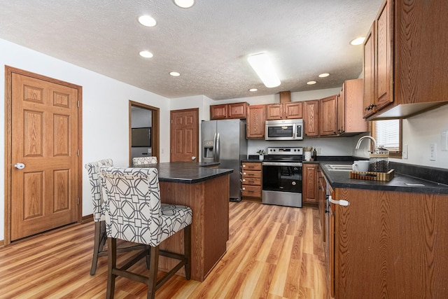 kitchen with brown cabinetry, dark countertops, appliances with stainless steel finishes, a breakfast bar area, and a sink