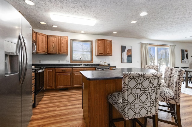 kitchen with stainless steel appliances, dark countertops, a kitchen island, a sink, and wood finished floors