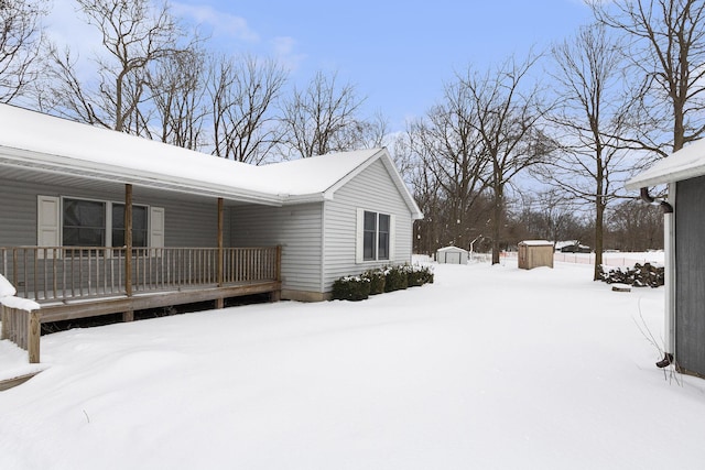 snow covered property with covered porch and a shed