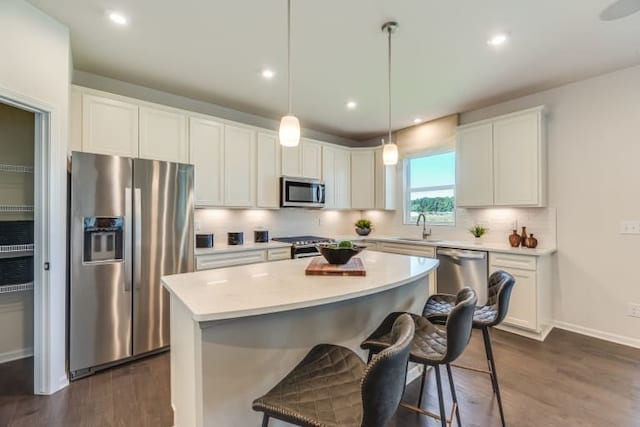 kitchen with white cabinetry, stainless steel appliances, a kitchen island, and hanging light fixtures