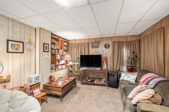 living room featuring a paneled ceiling, wood walls, and carpet