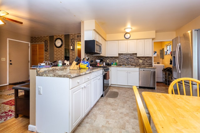 kitchen featuring sink, stainless steel appliances, kitchen peninsula, washer / dryer, and white cabinets