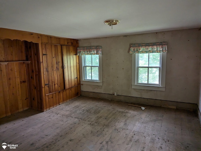 unfurnished room featuring a wealth of natural light, light hardwood / wood-style flooring, and wooden walls