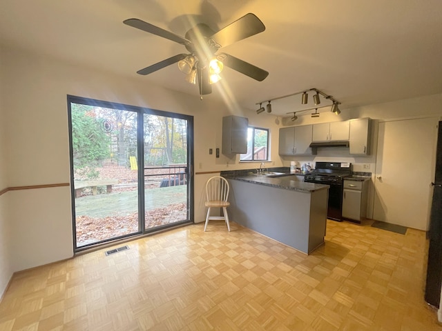 kitchen with ceiling fan, kitchen peninsula, black gas stove, light parquet floors, and gray cabinets