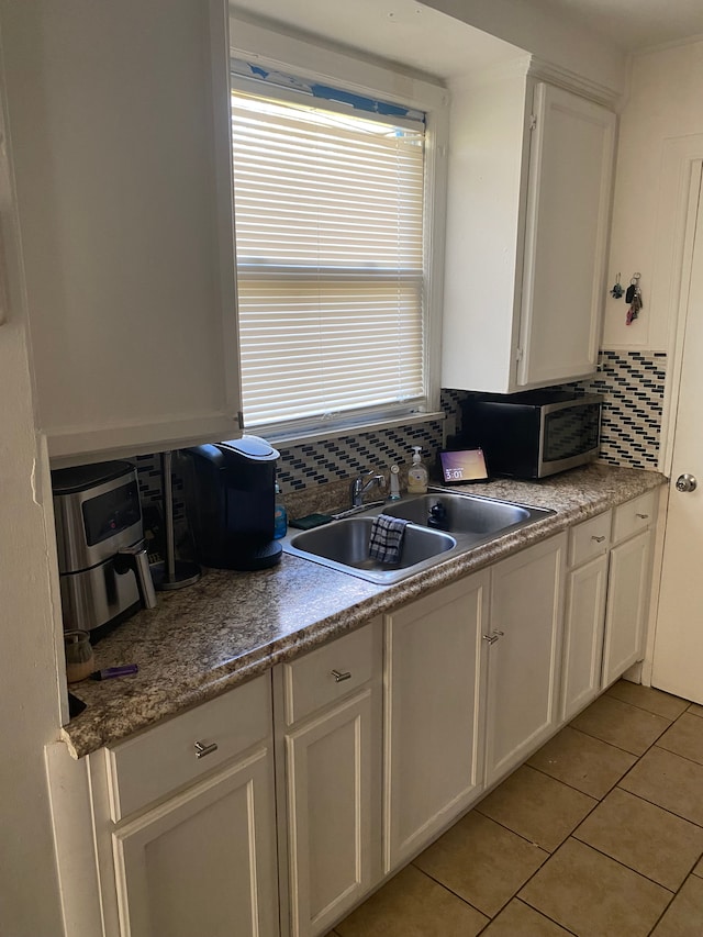 kitchen with decorative backsplash, light tile patterned floors, white cabinets, and sink