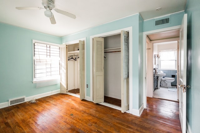 unfurnished bedroom with dark hardwood / wood-style flooring, two closets, ceiling fan, and ornamental molding