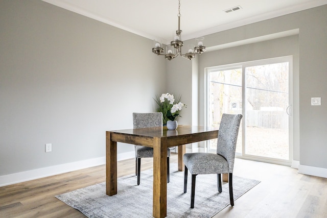 dining space with hardwood / wood-style flooring, crown molding, and a notable chandelier