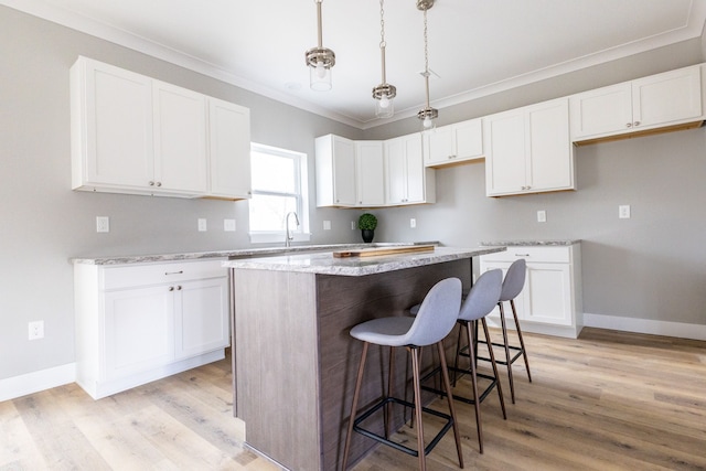 kitchen with crown molding, pendant lighting, white cabinets, a center island, and light hardwood / wood-style floors