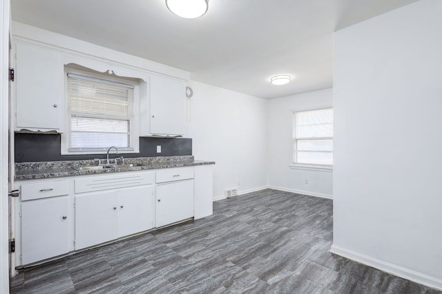 kitchen featuring dark countertops, baseboards, white cabinets, and a sink