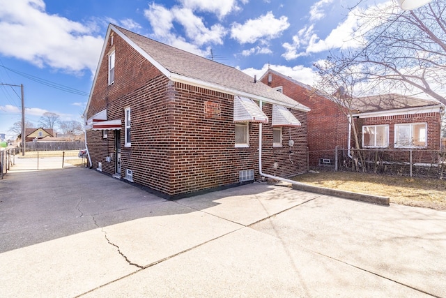 view of home's exterior featuring brick siding, fence, and roof with shingles