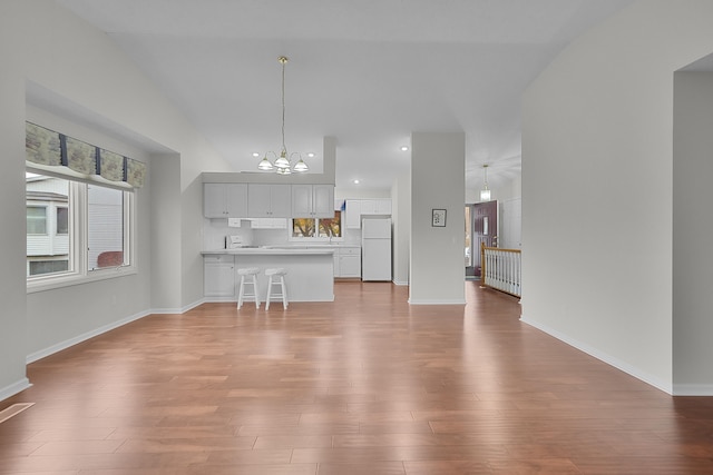 unfurnished living room featuring hardwood / wood-style floors, vaulted ceiling, and a chandelier