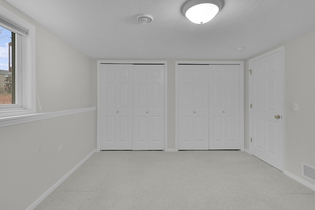 unfurnished bedroom with a textured ceiling, two closets, light carpet, and multiple windows