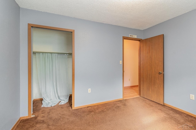 unfurnished bedroom featuring a textured ceiling, light carpet, and a closet