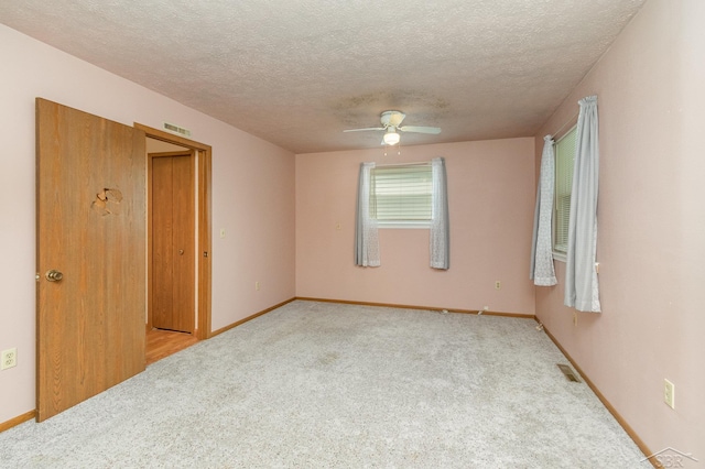 empty room featuring ceiling fan, a textured ceiling, and light carpet