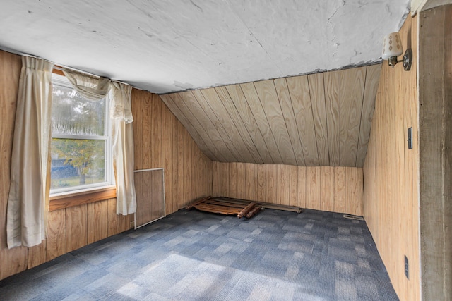 bonus room featuring vaulted ceiling, dark colored carpet, and wood walls