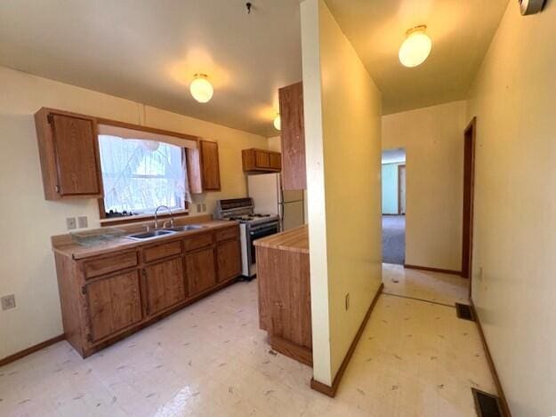 kitchen featuring visible vents, brown cabinets, a sink, gas range, and light floors