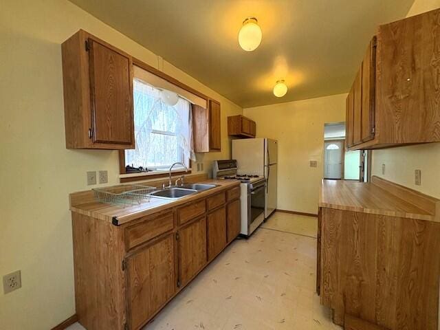 kitchen featuring baseboards, light floors, white range with gas stovetop, brown cabinets, and a sink