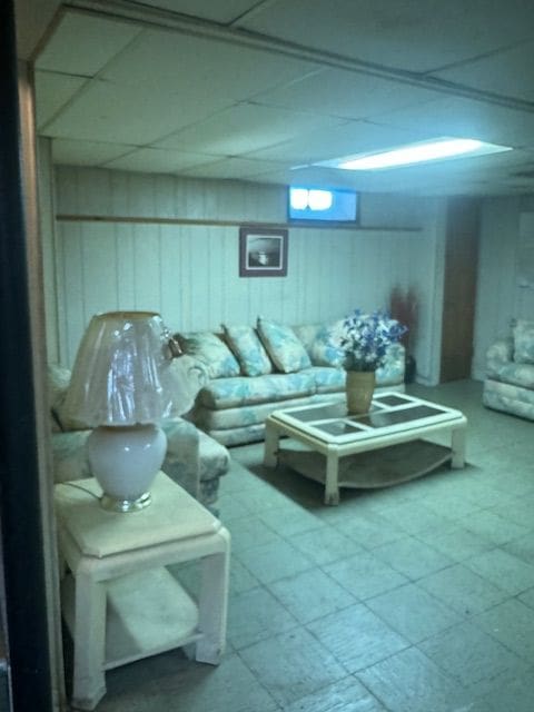 living room featuring a paneled ceiling, wood walls, and tile patterned floors