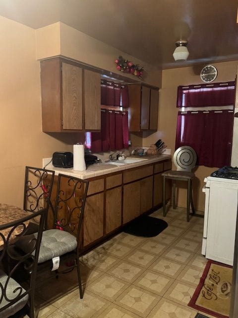 kitchen with light floors, white range with gas cooktop, a sink, and dark brown cabinets