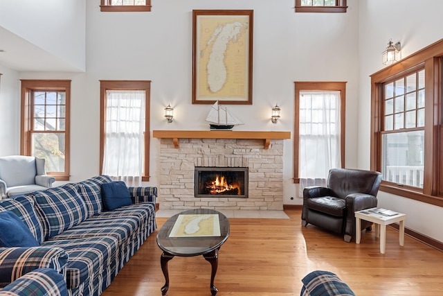 living room with a towering ceiling, light wood-type flooring, and a stone fireplace