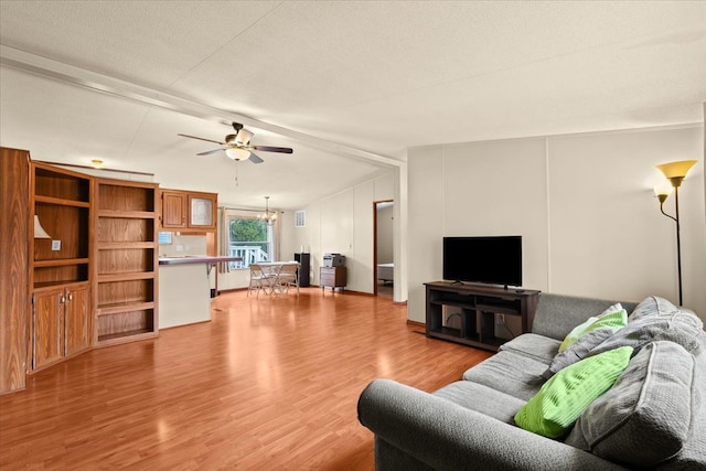 living room featuring ceiling fan with notable chandelier, beam ceiling, light wood-type flooring, and a textured ceiling