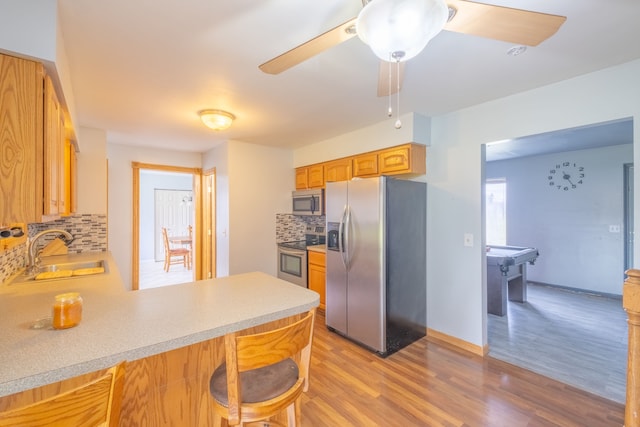 kitchen featuring sink, stainless steel appliances, backsplash, kitchen peninsula, and light hardwood / wood-style floors