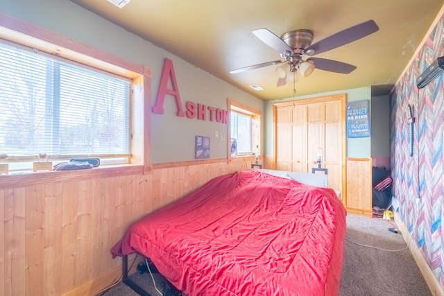 carpeted bedroom with ceiling fan, a closet, and wood walls