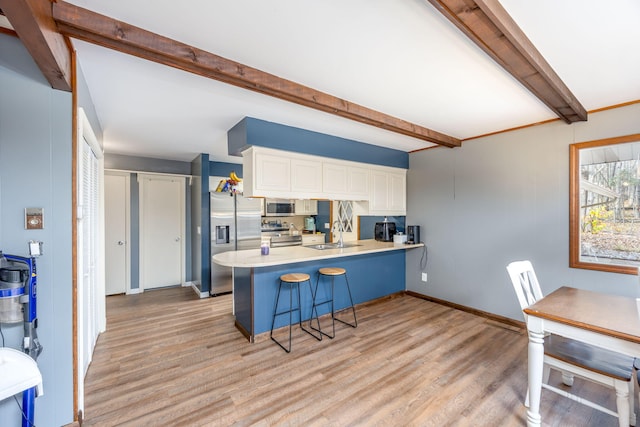 kitchen with white cabinets, appliances with stainless steel finishes, beamed ceiling, light hardwood / wood-style floors, and kitchen peninsula