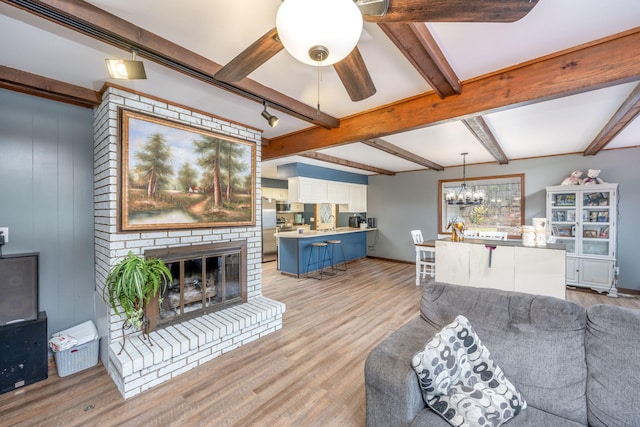 living room featuring ceiling fan with notable chandelier, sink, a brick fireplace, light hardwood / wood-style flooring, and beam ceiling