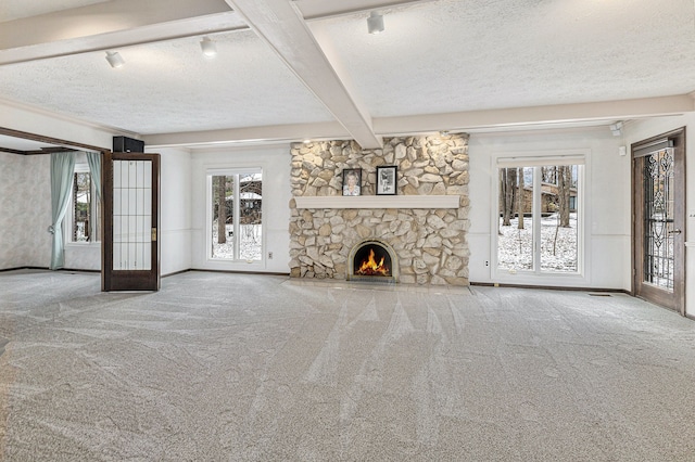 unfurnished living room with french doors, beamed ceiling, a textured ceiling, a fireplace, and carpet