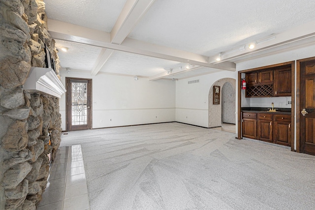 unfurnished living room featuring beamed ceiling, wet bar, a textured ceiling, and light carpet