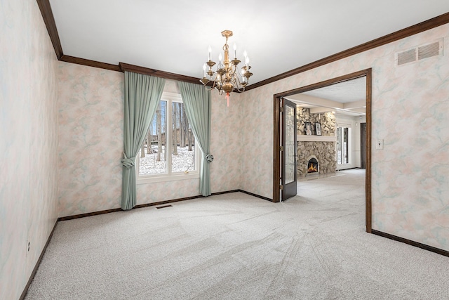 empty room with carpet, a stone fireplace, crown molding, and a chandelier