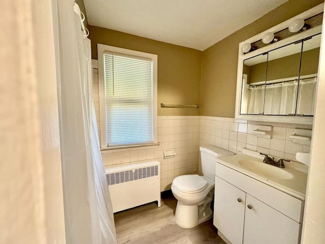 bathroom featuring vanity, hardwood / wood-style flooring, toilet, tile walls, and radiator heating unit