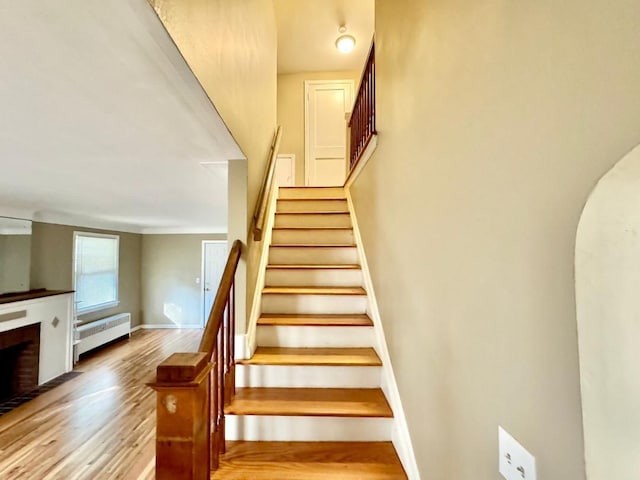 stairway featuring hardwood / wood-style floors, a brick fireplace, and radiator