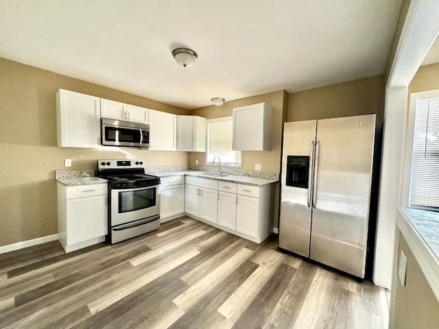 kitchen with white cabinetry, sink, light stone counters, light hardwood / wood-style floors, and appliances with stainless steel finishes