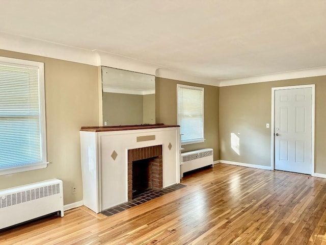 unfurnished living room featuring hardwood / wood-style floors, a brick fireplace, radiator, and ornamental molding