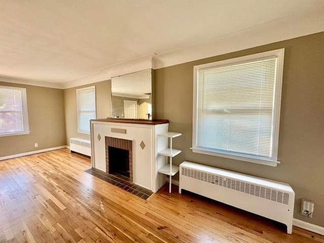 unfurnished living room featuring light wood-type flooring, radiator heating unit, and a brick fireplace