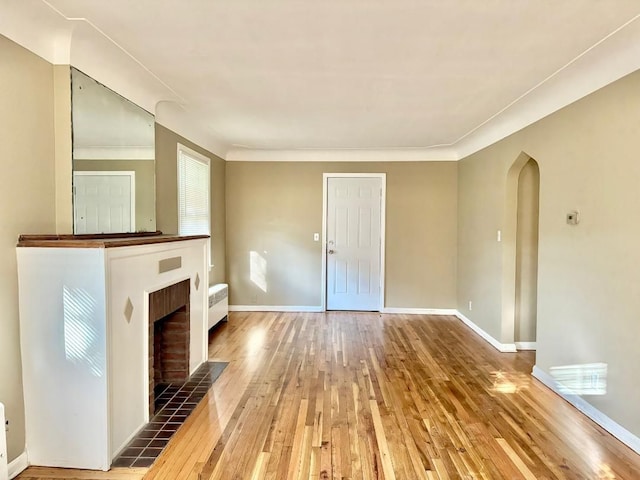 unfurnished living room with wood-type flooring, crown molding, and a tiled fireplace