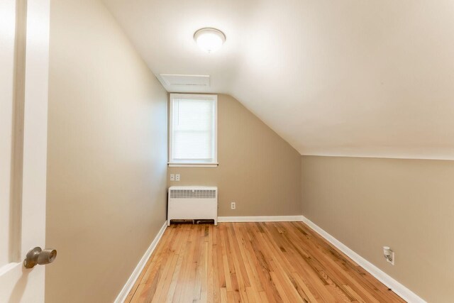 additional living space featuring radiator heating unit, lofted ceiling, and light hardwood / wood-style flooring