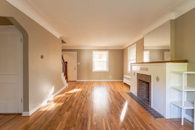 unfurnished living room with hardwood / wood-style floors, radiator heating unit, and a brick fireplace