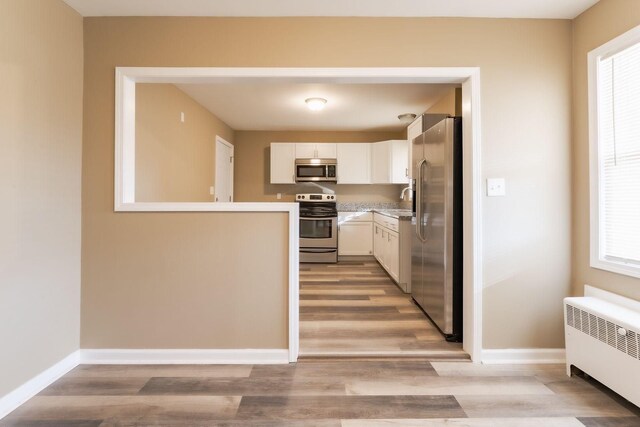 kitchen with white cabinets, stainless steel appliances, plenty of natural light, and radiator