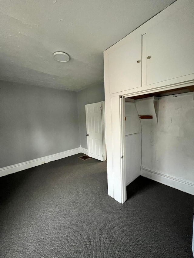 unfurnished bedroom featuring dark carpet, a textured ceiling, and a closet