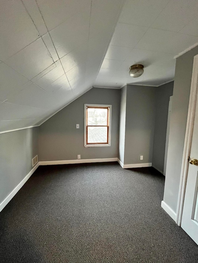 additional living space featuring dark colored carpet and vaulted ceiling