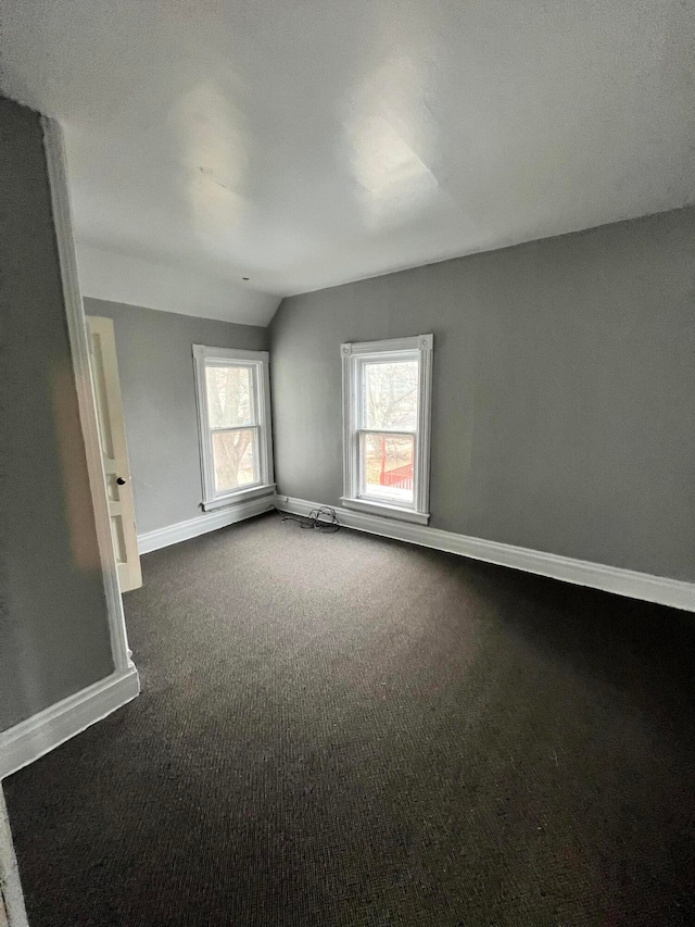 empty room featuring lofted ceiling and dark colored carpet