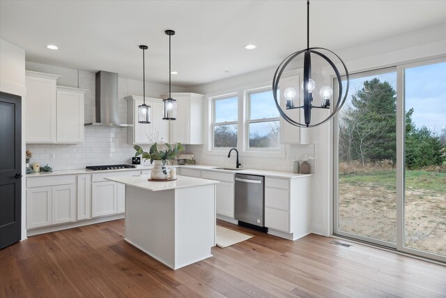 kitchen featuring decorative light fixtures, sink, white cabinets, stainless steel dishwasher, and wall chimney range hood